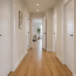 Pasillo de vivienda con varias puertas de interior blancas y suelo de madera, salón al fondo