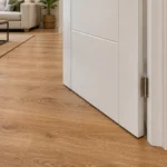 Puerta de interior blanca junto a suelo laminado en tono madera, con salón al fondo