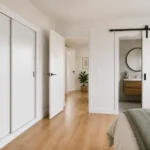 Dormitorio con armario de puertas correderas abierto y puerta corredera tipo granero hacia el baño